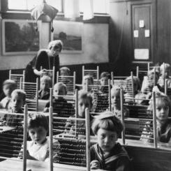 Schoolklas poseert met de handen ineengevouwen en telramen op tafel, circa 1930.